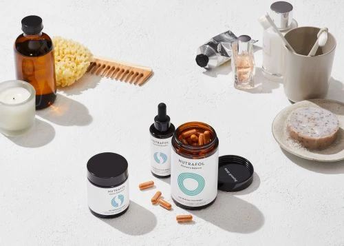 Still life of various self-care and hair supplement items including bottles, pills, and personal care products arranged on a white surface.