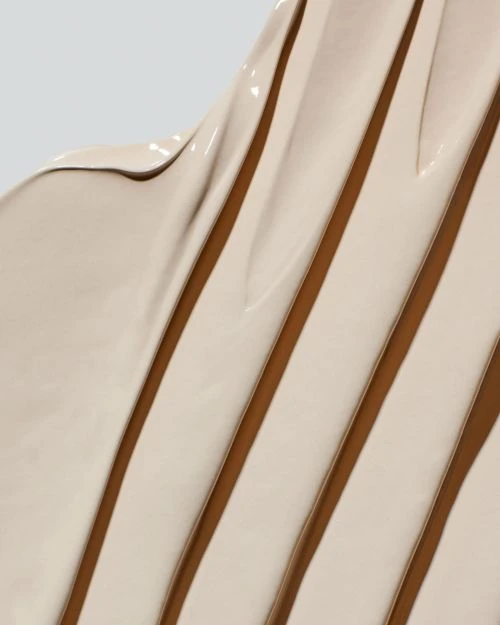 Macro shot of beige cosmetic product reveals a thick, creamy texture with parallel darker brown stripes. Glossy surface, neutral color palette.