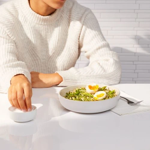 Woman at table with white bowl of salad with soft-boiled eggs and salt, brick wall background with natural window light.