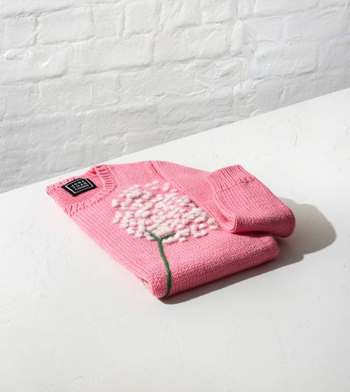 Folded pink knit sweater with a white floral appliqué and green stem resting on a white surface.