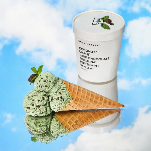 Daily Harvest ice cream pint with an ice cream cone filled with ice cream and garnished with mint leaves against a sky backdrop.