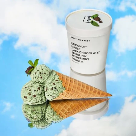 Daily Harvest ice cream pint with an ice cream cone filled with ice cream and garnished with mint leaves against a sky backdrop.