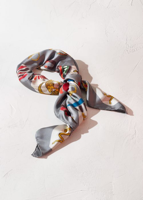 Silk scarf with intricate patterns on a textured white surface, artful arrangement, fashion accessory, and soft studio lighting.