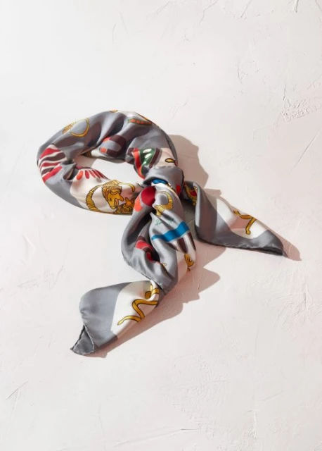 Silk scarf with intricate patterns on a textured white surface, artful arrangement, fashion accessory, and soft studio lighting.