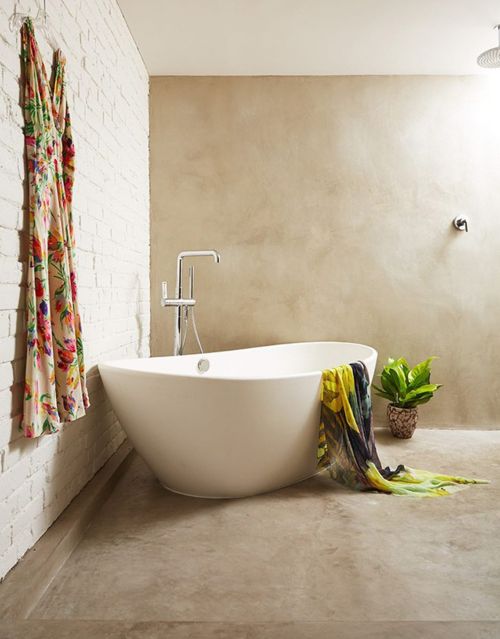 Contemporary bathroom features a standalone white bathtub, neutral wall tones, a hanging floral dress, and indoor potted plants.