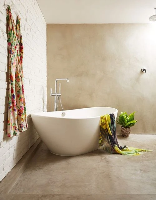 Contemporary bathroom features a standalone white bathtub, neutral wall tones, a hanging floral dress, and indoor potted plants.