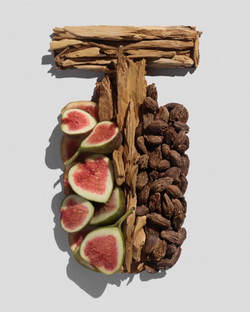 Still life composition featuring figs, assorted woods, and spices arranged in a T-shape on a soft gray background, high-angle.