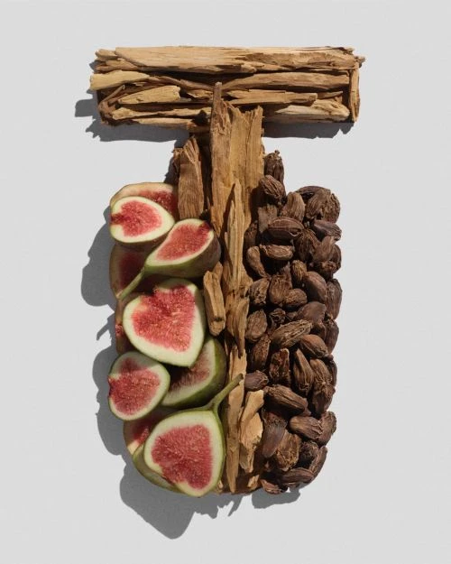 Still life composition featuring figs, assorted woods, and spices arranged in a T-shape on a soft gray background, high-angle.