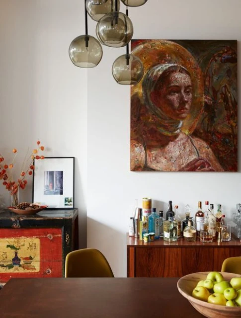 Interior dining area featuring a portrait painting, modern chandelier, vintage cabinet, dining table, and chairs in a home setting.