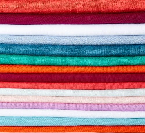 Stack of folded textile in orange, maroon, and blue tones forming a colorful, textured background. Fabric is closely arranged in layers.