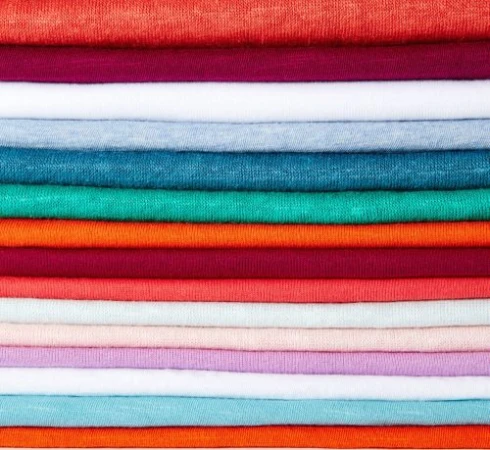 Stack of folded textile in orange, maroon, and blue tones forming a colorful, textured background. Fabric is closely arranged in layers.
