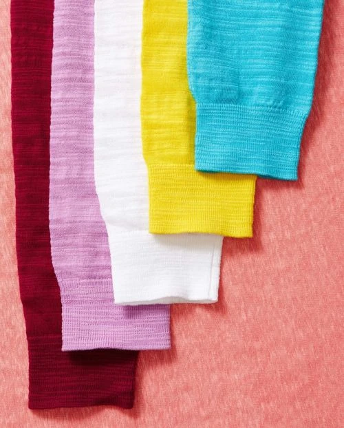 Closeup of colorful ribbed knit fabric swatches in red, pink, white, yellow, and turquoise stacked against a textured pink background.