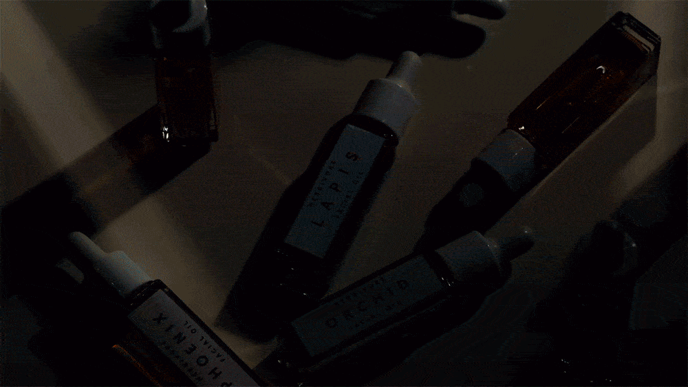 Several Neubrow Lapis and Phoenix facial oil dropper bottles on a surface with a dark and muted color palette. 
