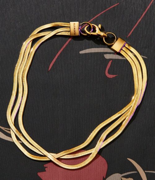 Gold multi-strand herringbone chain necklace on a dark background with abstract floral design, fashion jewelry close-up.