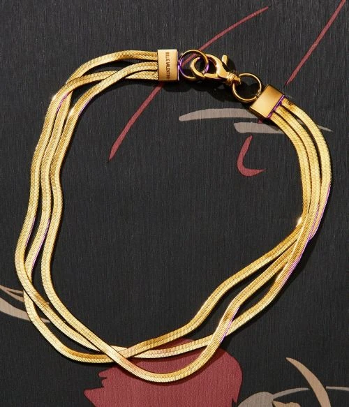 Gold multi-strand herringbone chain necklace on a dark background with abstract floral design, fashion jewelry close-up.
