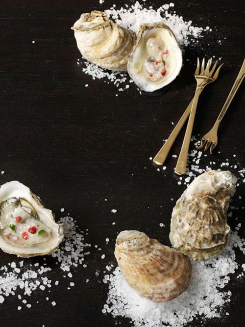 Overhead shot of oysters on the half shell with forks and sea salt scattered on a dark wooden surface, food photography. 