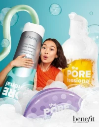 A smiling woman holding a giant cosmetic tube amidst soap bubbles, styled by Rebecca Donnelly