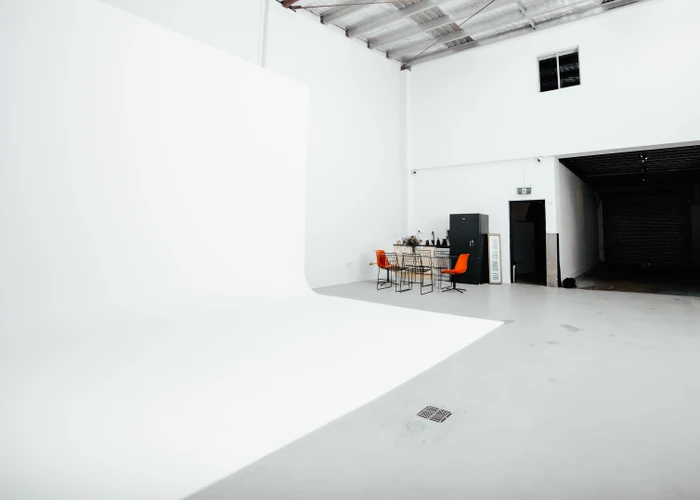 Spacious white photo studio interior featuring a large white cyclorama wall, concrete floor, and orange chairs in Sydney by Uno Studios.