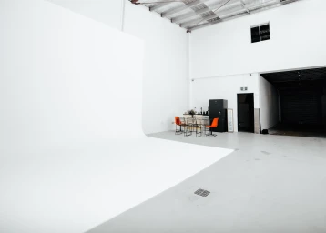 Spacious white photo studio interior featuring a large white cyclorama wall, concrete floor, and orange chairs in Sydney by Uno Studios.