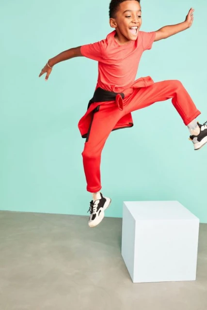 Joyful young boy in red athletic wear leaps mid-air in a bright studio setting, filled with energy and playful movement.