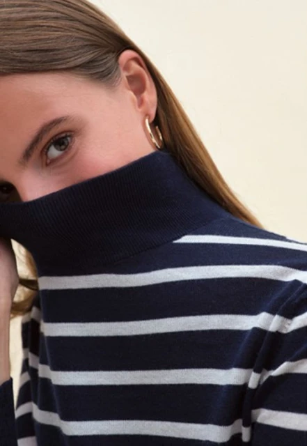 Close-up portrait of a young adult female with brown hair and blue eyes wearing a navy and white striped turtleneck sweater.