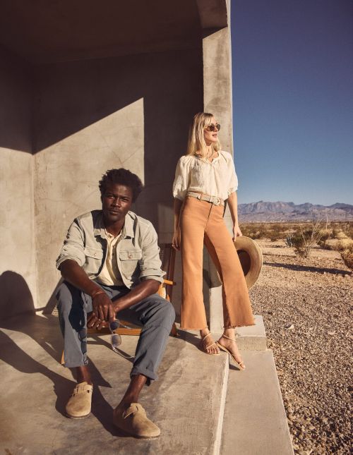 Man seated on concrete porch steps and woman standing beside him in desert landscape styled by Tennille Yamashita.