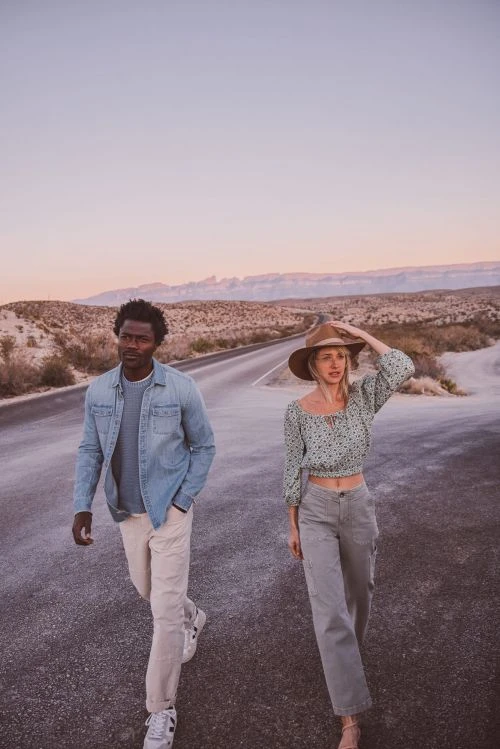 Man and woman walking along a desert road at sunset with distant hills, styled by Tennille Yamashita