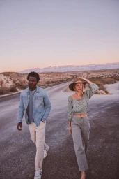 Man and woman walking along a desert road at sunset with distant hills, styled by Tennille Yamashita