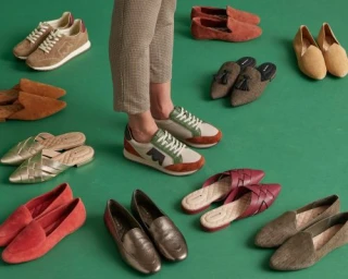 Person standing amidst a collection of various shoes on a green backdrop styled by Tennille Yamashita