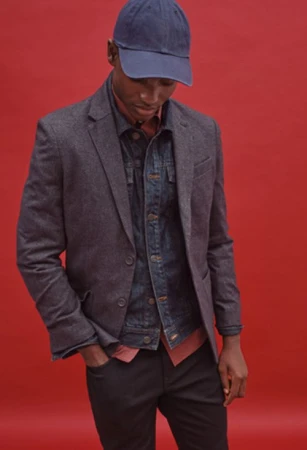 Man wearing a dark blazer, denim jacket, and blue cap against a red background, styled by Tennille Yamashita