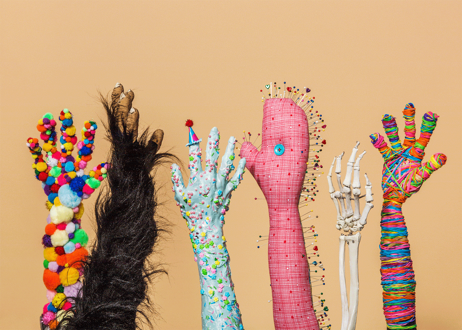 Creative studio shot of five decorated human-like hands, each with unique themes like fur, pompoms, pins, and colorful bands, on beige backdrop.