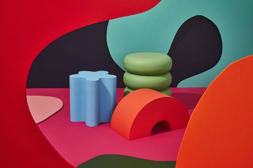 Abstract product shot with geometric shapes in red, orange, blue and green arranged on a fuchsia-colored surface, studio setting.