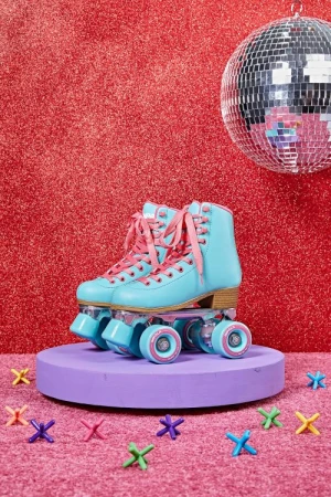 A pair of vintage turquoise roller skates are displayed on a purple platform against a red glitter backdrop with a disco ball.