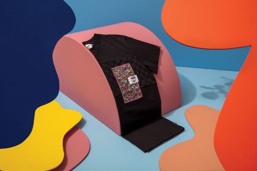 Black Vans t-shirt with floral pocket detail, styled on a pink curved display against a blue backdrop with abstract shapes.