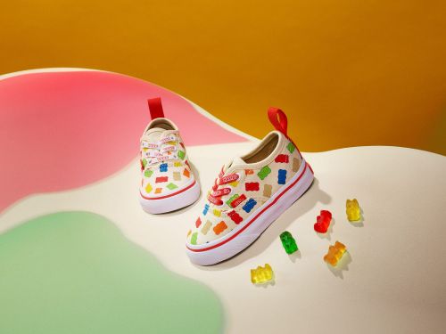Two pairs of toddler canvas sneakers featuring colorful gummy bear shapes are placed on a colorful pink, green, and yellow surface.