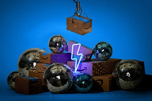 Stack of Amazon boxes and disco balls under a claw game crane arm, lit with a neon lightning bolt against a blue background.