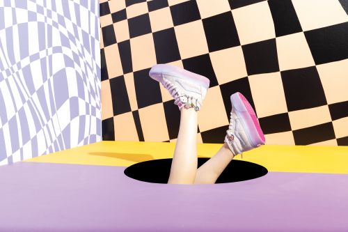 Person's legs and white sneakers sticking out of a hole in a floor with black, white, and yellow geometric background.