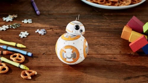 Toy robot on wooden table with crayons, puzzle pieces, pretzels, and colored blocks creates a playful, colorful scene for children.