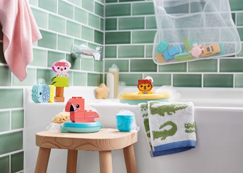 Fun assortment of animal-themed bath toys arranged by a white bathtub with light green tile in a brightly lit bathroom scene.