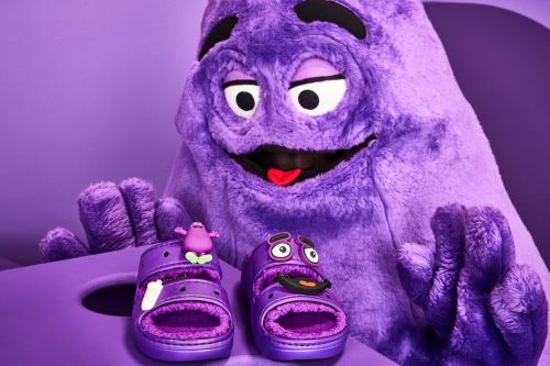 Grimace character with purple Crocs and Grimace Jibbitz in a studio setup with a purple background. Cartoon-inspired fashion photography.