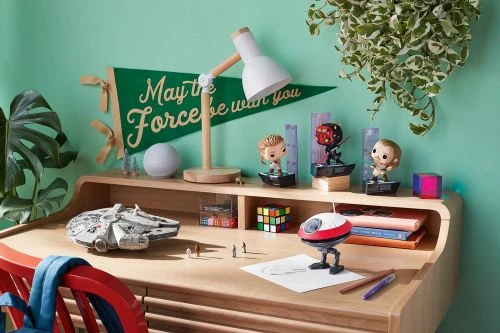 Desk with Star Wars collectibles: Millennium Falcon model, figures, lamp, Rubik's Cube, books, pencils, and a pennant on a desk.