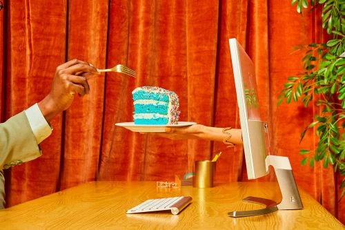 Hands reach out from a computer screen to offer a slice of cake, highlighting digital connectivity and food presentation.