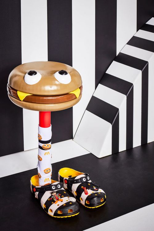 Whimsical product shot of Crocs sandals with a McDonald's theme, presented with a hamburger-shaped seat on a black and white background.