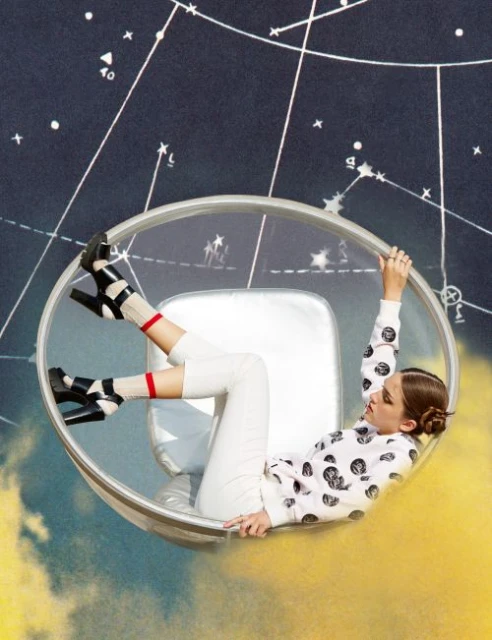 Woman in white outfit and black heels sits in clear chair against constellation background and yellow clouds. Fashion and style concept.