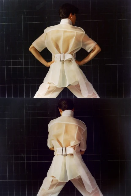 Two images of a person in a white, translucent short-sleeved shirt, belt and pants, standing with hands on hips against a black tile wall.