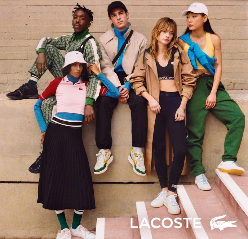 Group of five fashion models pose on stairs in casual clothing for a Lacoste advertisement. Bright, colorful clothing is featured.