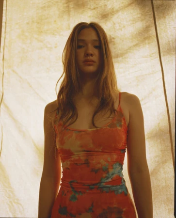 Portrait of a young woman with long hair in a tie-dye dress against a textured cream-colored fabric backdrop in a photo studio.