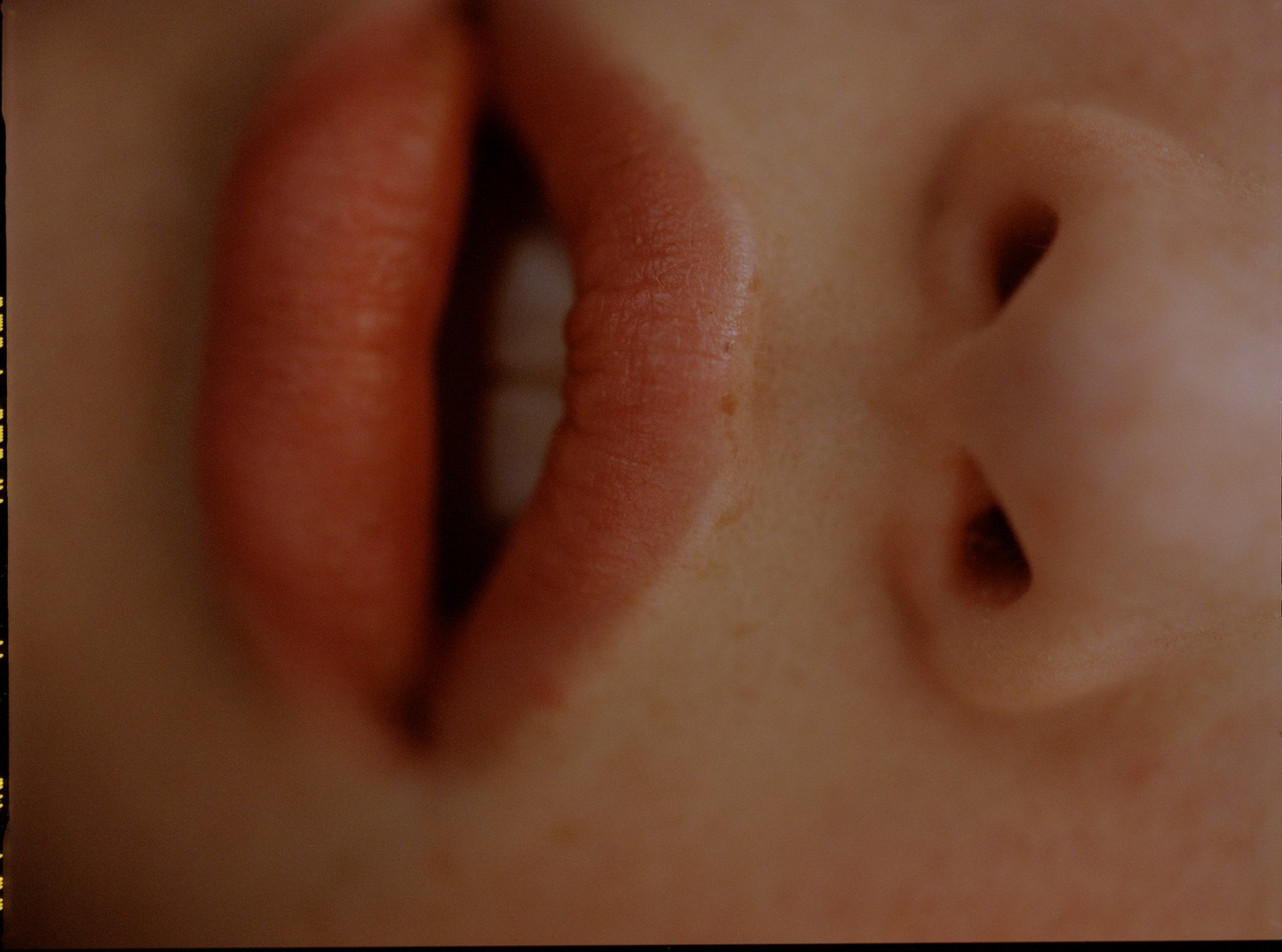 Extreme close-up of a person's face showing lips, teeth, and nose in a warm-toned, soft-focus composition, emphasizing skin texture.