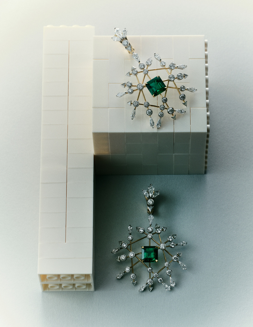 Emerald and diamond earrings on a white and grey surface, jewelry still life, indoor studio lighting, high-end jewelry, gemstone earrings.