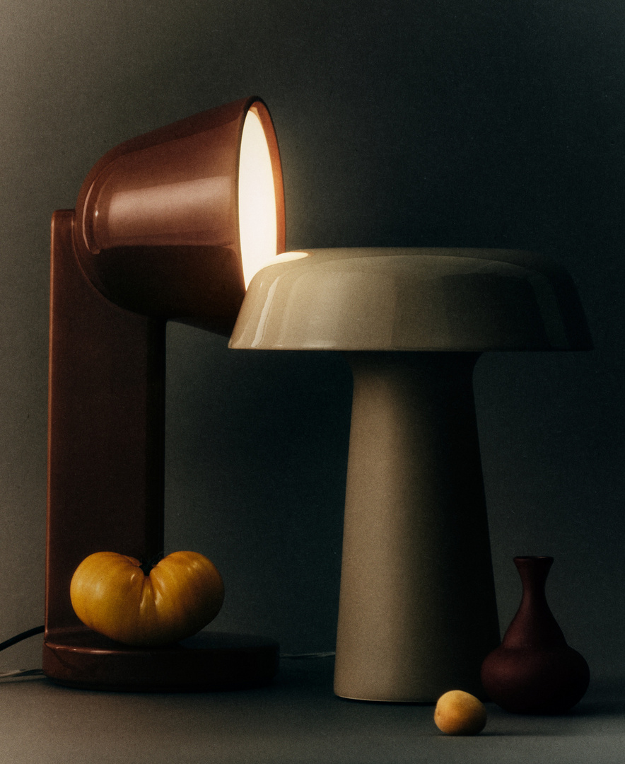 Still life featuring two table lamps in a photo studio setting, with a small vase and fruits on a neutral-colored surface.